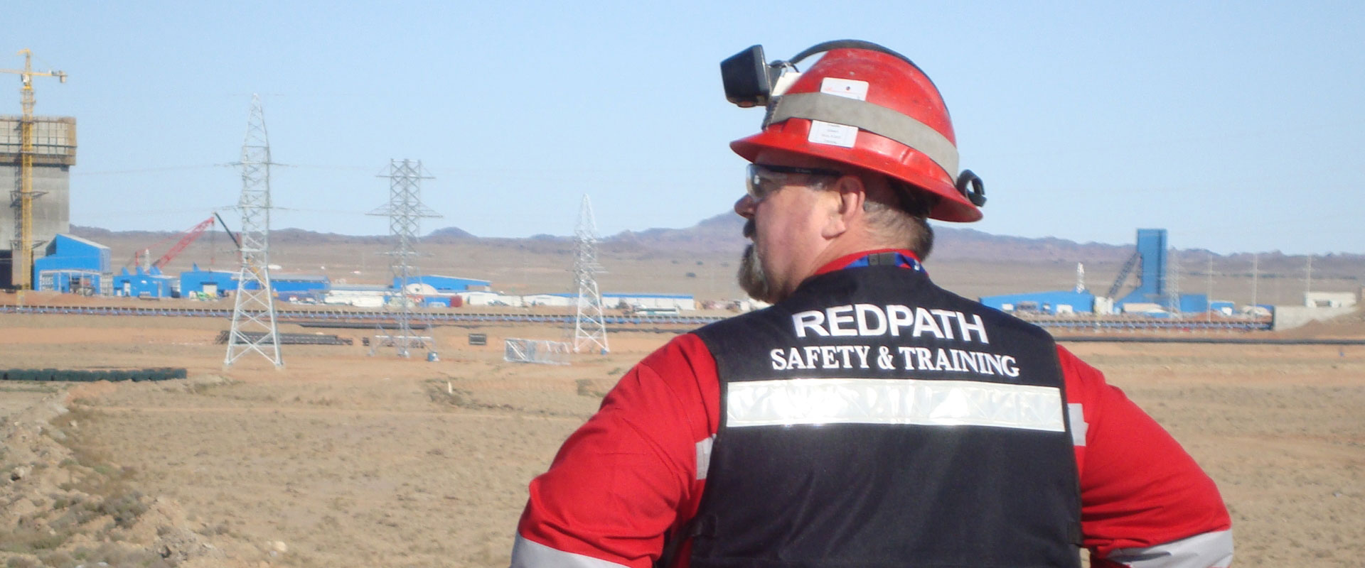 A Redpath employee in the Safety & Training division, wearing safety equipment, is inspecting the ground level of a mine site.