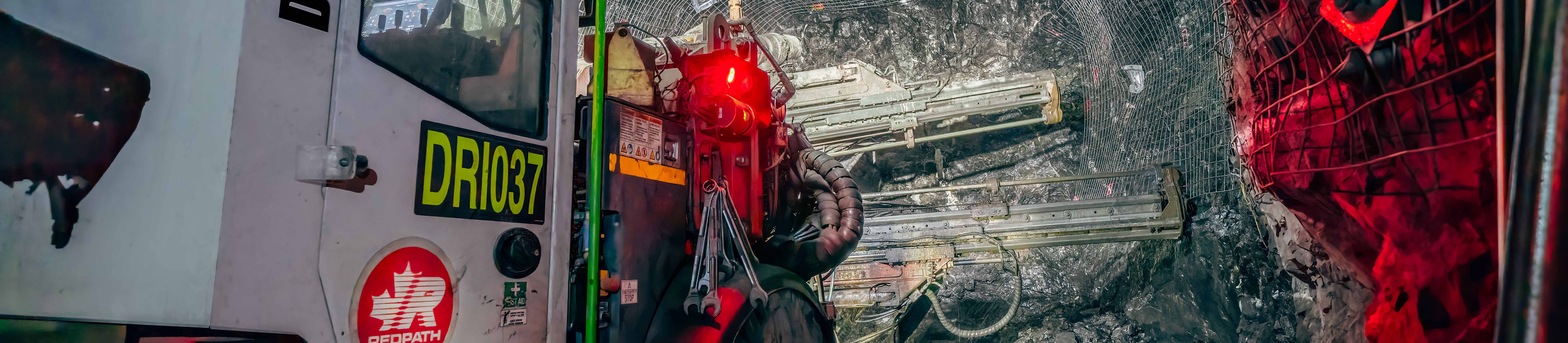 El banner del sitio web para la página de noticias recientes muestra un taladro de pernos Redpath que aplica una malla de alambre en las paredes y el techo de un túnel subterráneo.