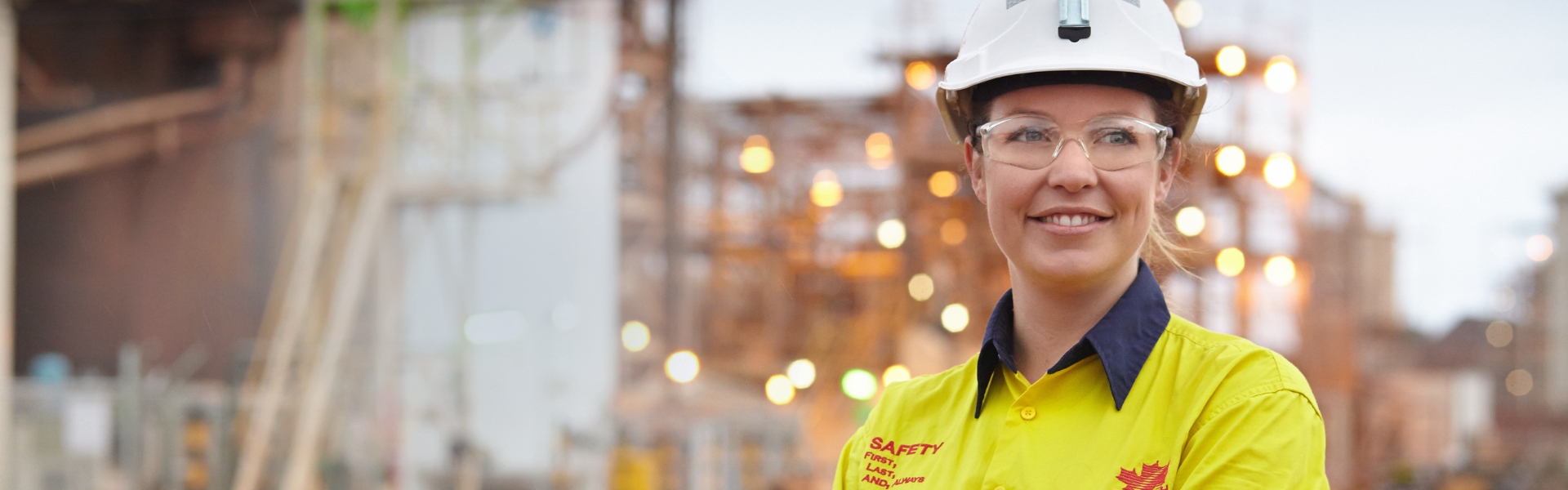 Smiling Redpath employee above ground with lights from a mine site in the background.