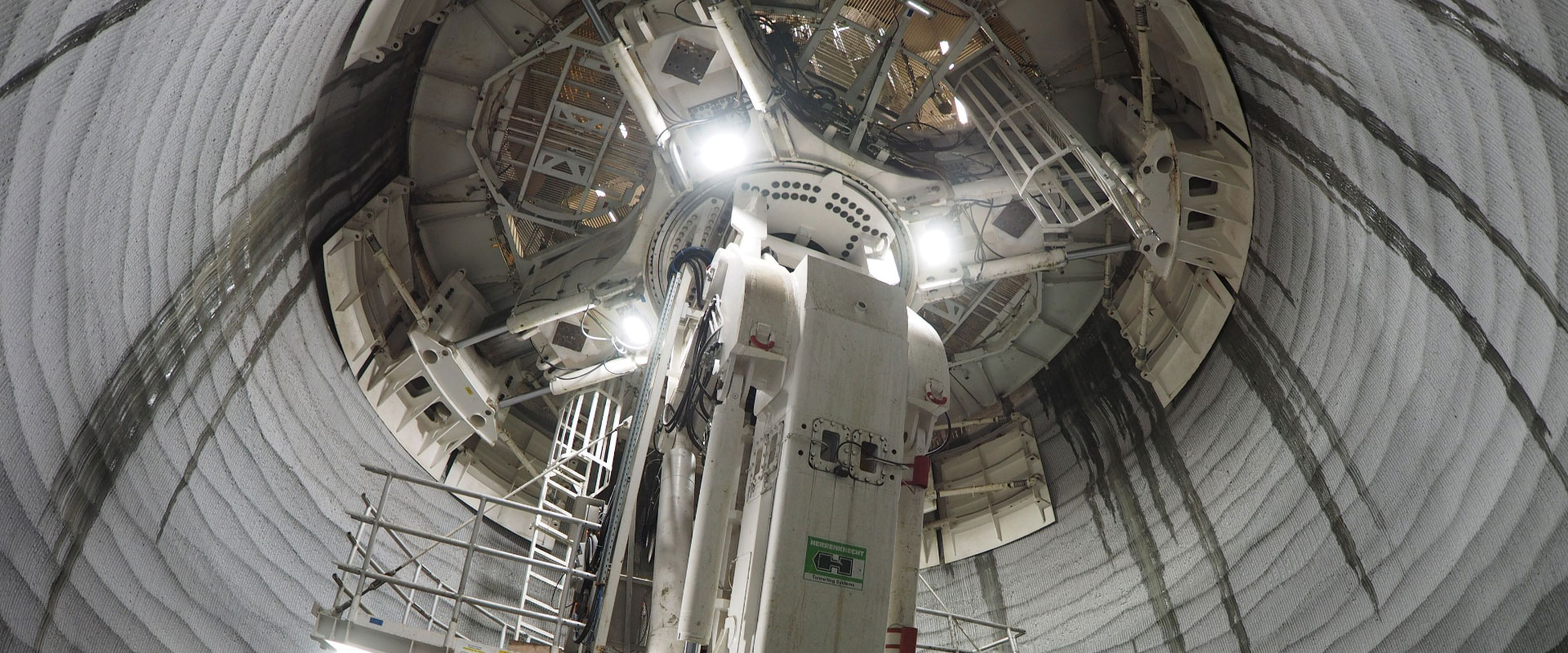 Una m&aacute;quina taladradora de t&uacute;neles es una pieza compleja de ingenier&iacute;a, con varios componentes visibles: un cabezal de corte o escudo en la parte delantera, soportes hidr&aacute;ulicos y una red de cables y plataformas de acceso.